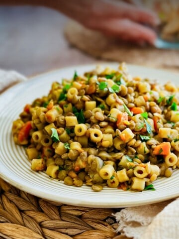 Cooked lentils and ditalini pasta on a plate with someone putting a bowl of salad down in the background.