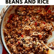 Pinterest pin graphic for Mexican Black Beans and Rice showing a wooden spoon scooping fluffy seasoned rice and black beans from a red dutch oven, with the text "How to Make Mexican Black Beans and Rice" and nutsandtwigs.com.