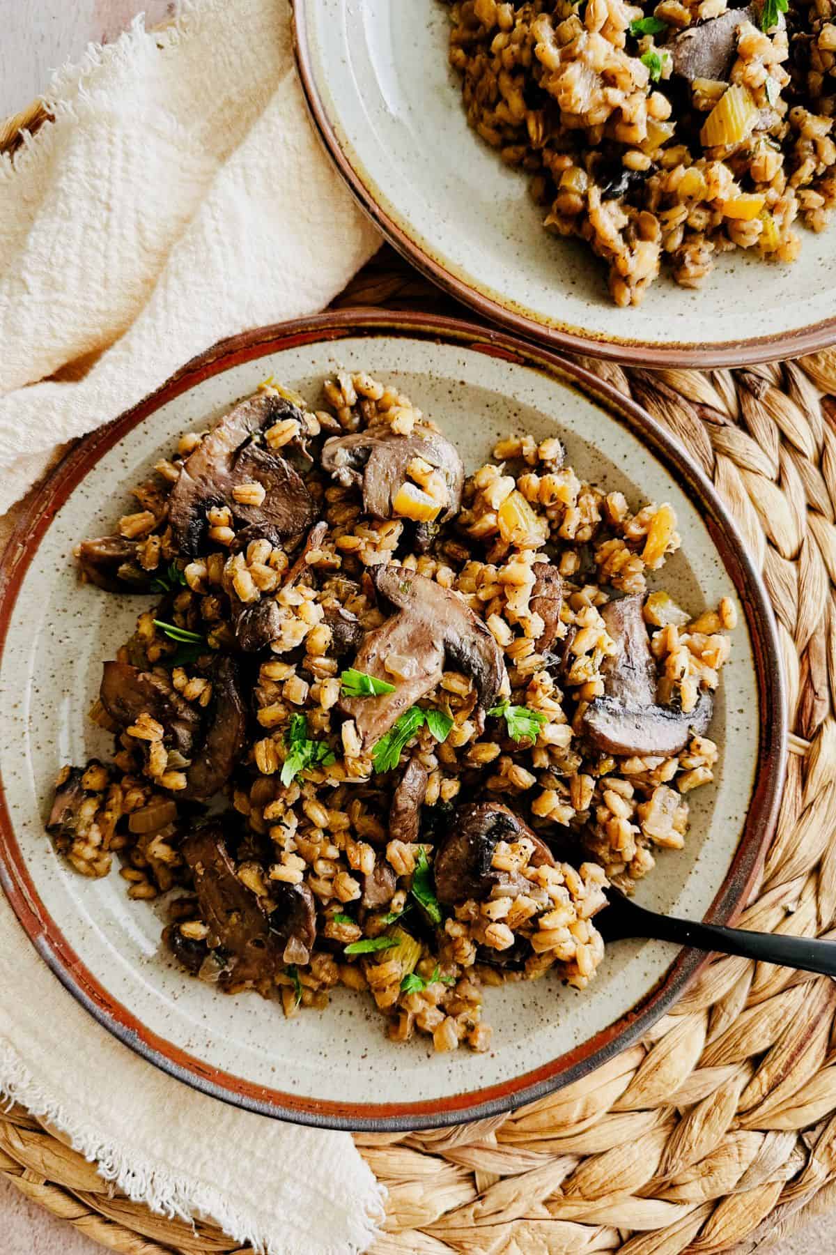 Two plates of mushroom barley pilaf garnished with fresh parsley.