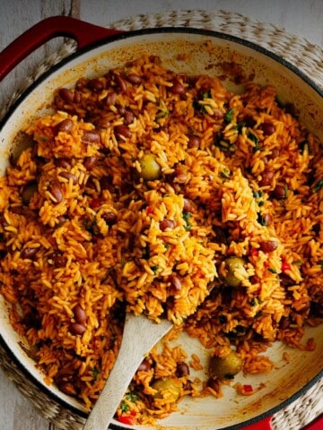 Top view of Puerto Rican Yellow Rice and Beans in a red dutch oven with a wooden spoon in the rice.