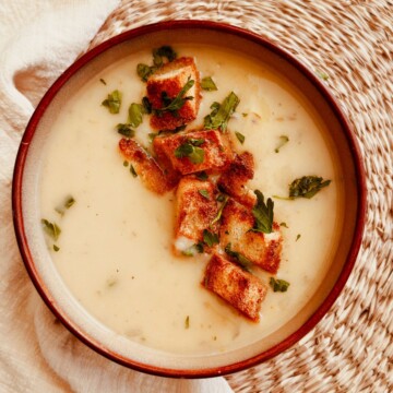 Roasted Garlic and Potato soup in a bowl topped with croutons and chopped parsley.