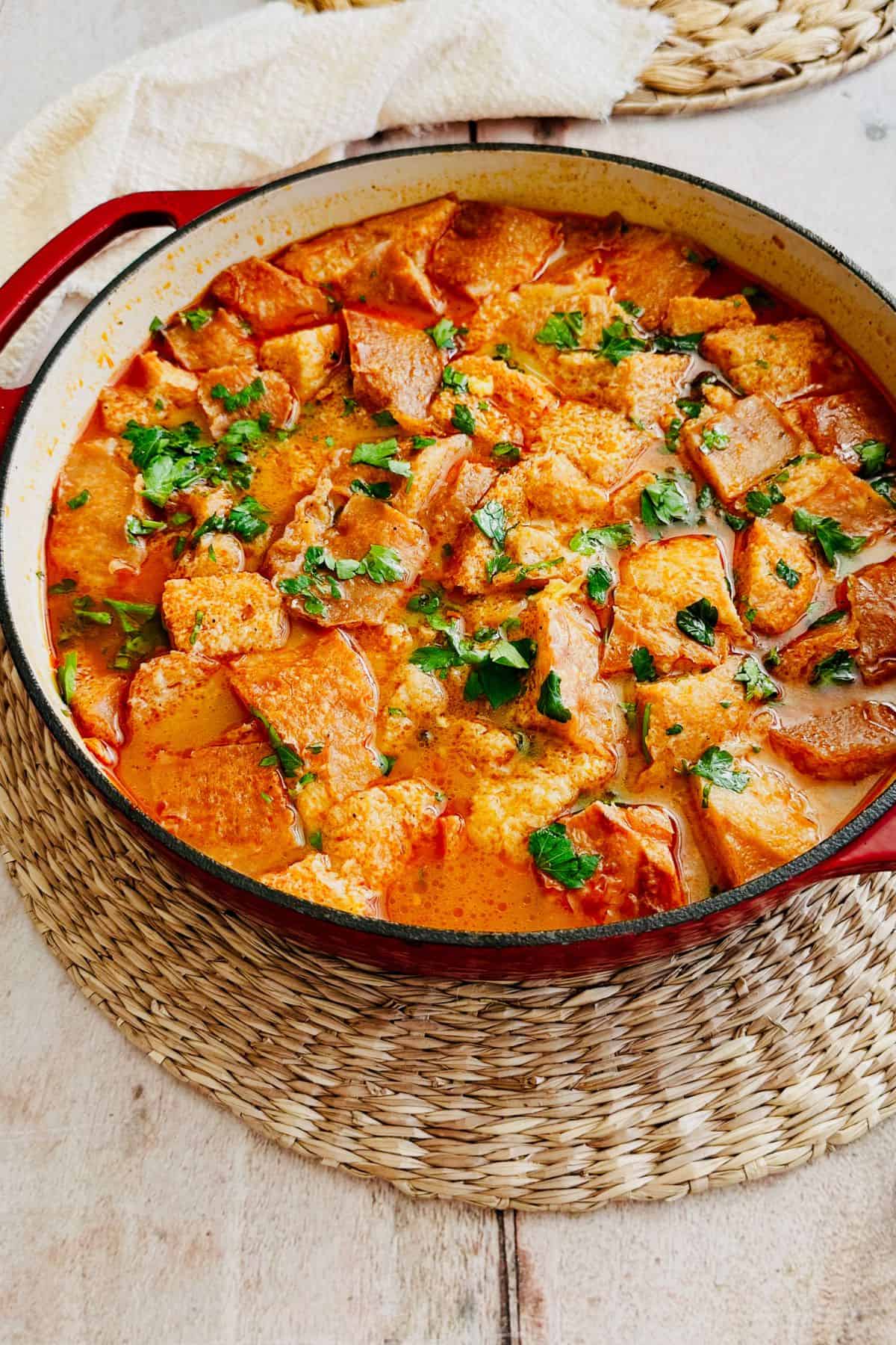 Spanish garlic soup (sopa de ajo) in a red Dutch oven with chunks of crusty bread and fresh parsley.