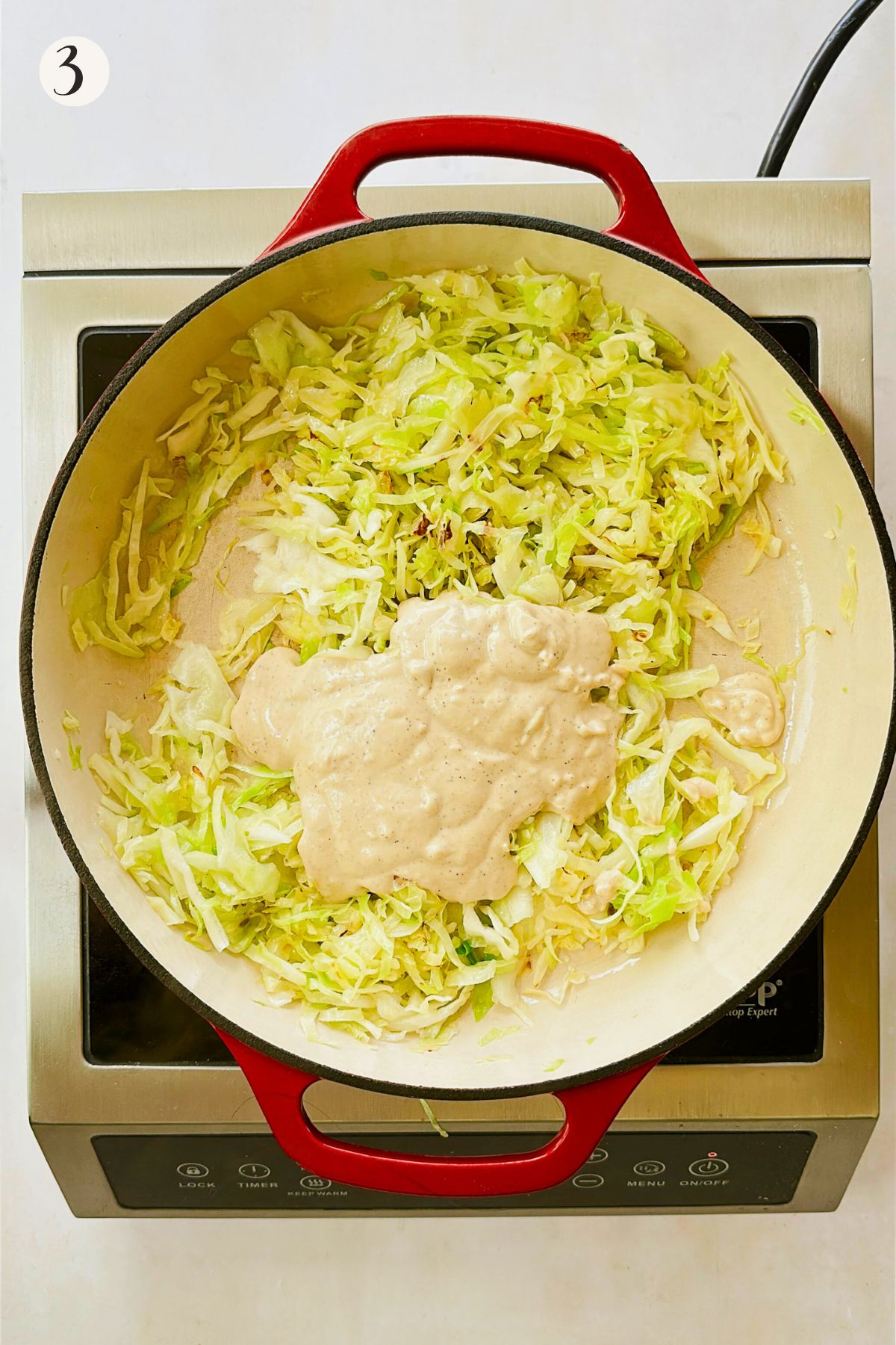 Creamy cashew alfredo sauce poured over sautéed cabbage in a red Dutch oven.