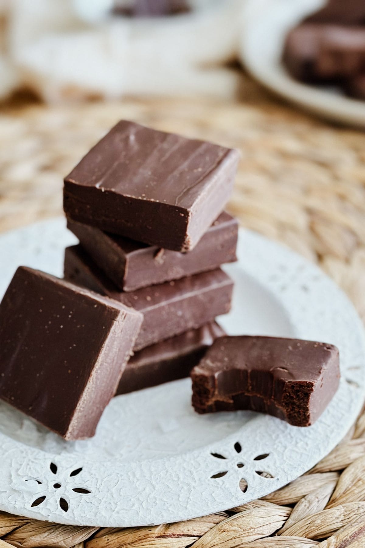 Stack of creamy vegan fudge squares on a plate with one piece bitten to show the smooth texture.