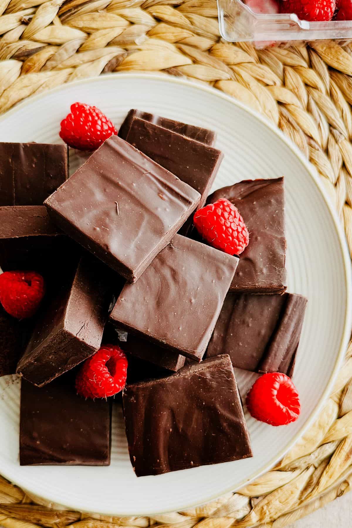Squares of vegan chocolate fudge on a white plate garnished with fresh raspberries.