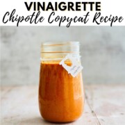 A mason jar filled with smooth, smoky chipotle vinaigrette and a handwritten label, sitting on a rustic wood surface with text overlay reading 'How to Make Chipotle Vinaigrette — Chipotle Copycat Recipe' from NutsandTwigs.com.