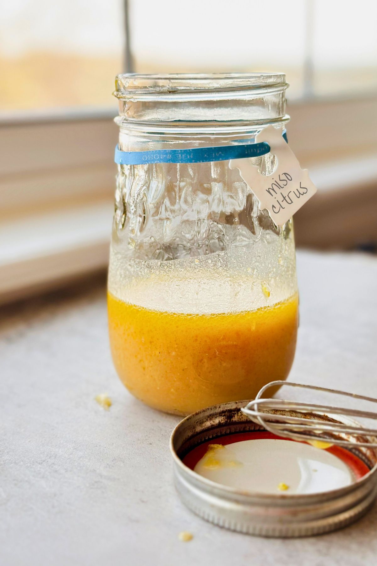 Glass jar of miso citrus vinaigrette with a light orange color, partially emulsified, labeled 