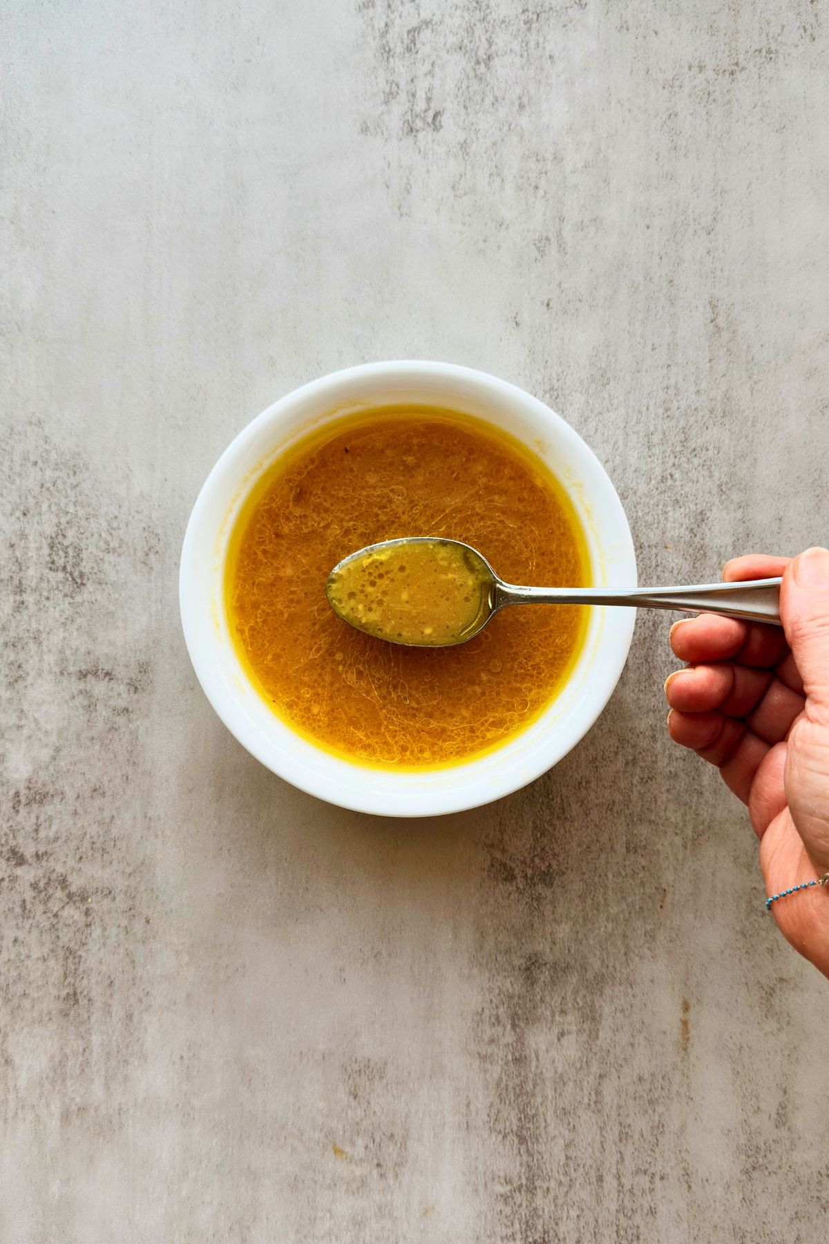Small white bowl of golden miso citrus dressing with a spoon showing its smooth, slightly textured consistency from above.