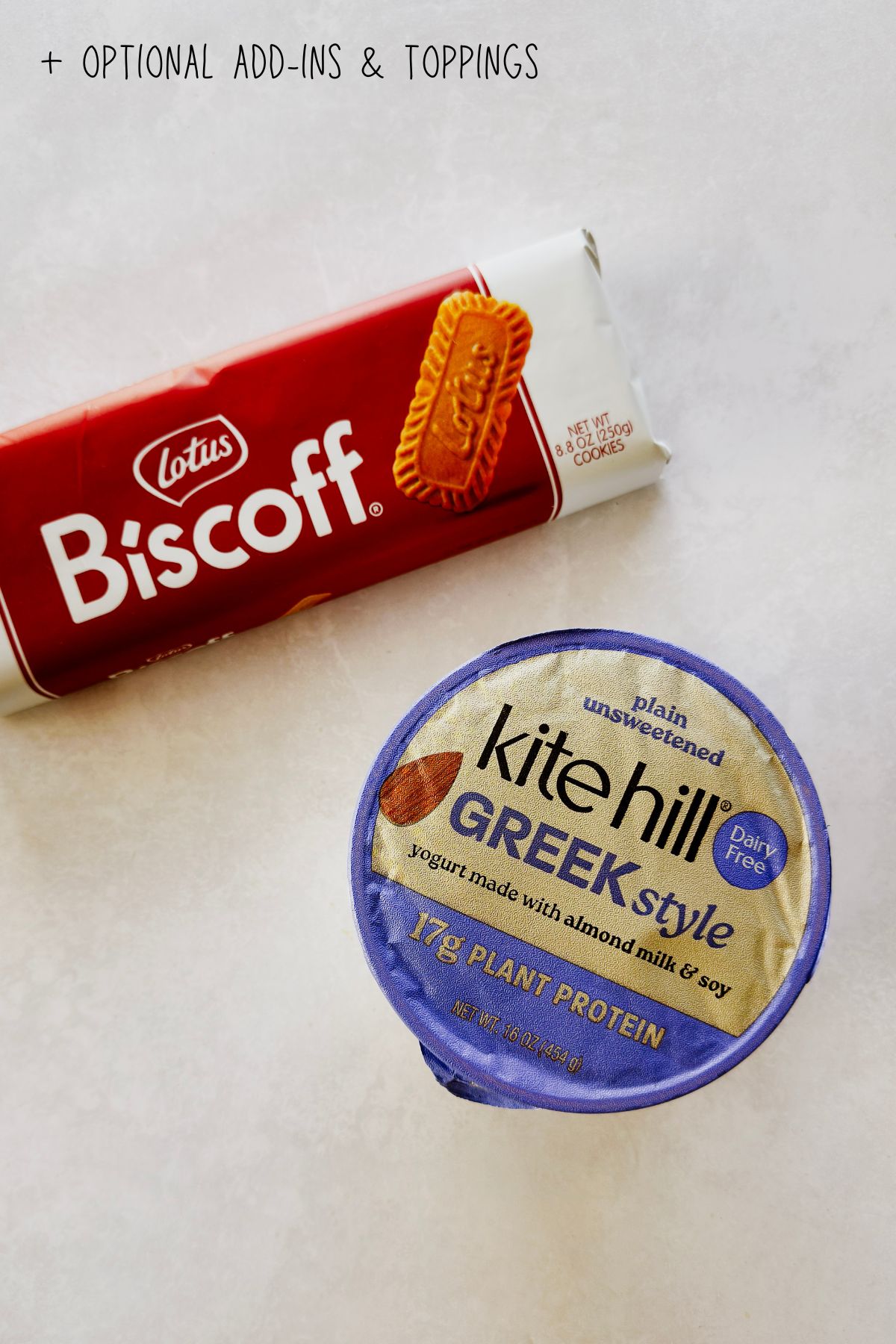 Kite Hill Greek style vegan yogurt and Lotus Biscoff cookies on a white surface with text reading optional add-ins and toppings.