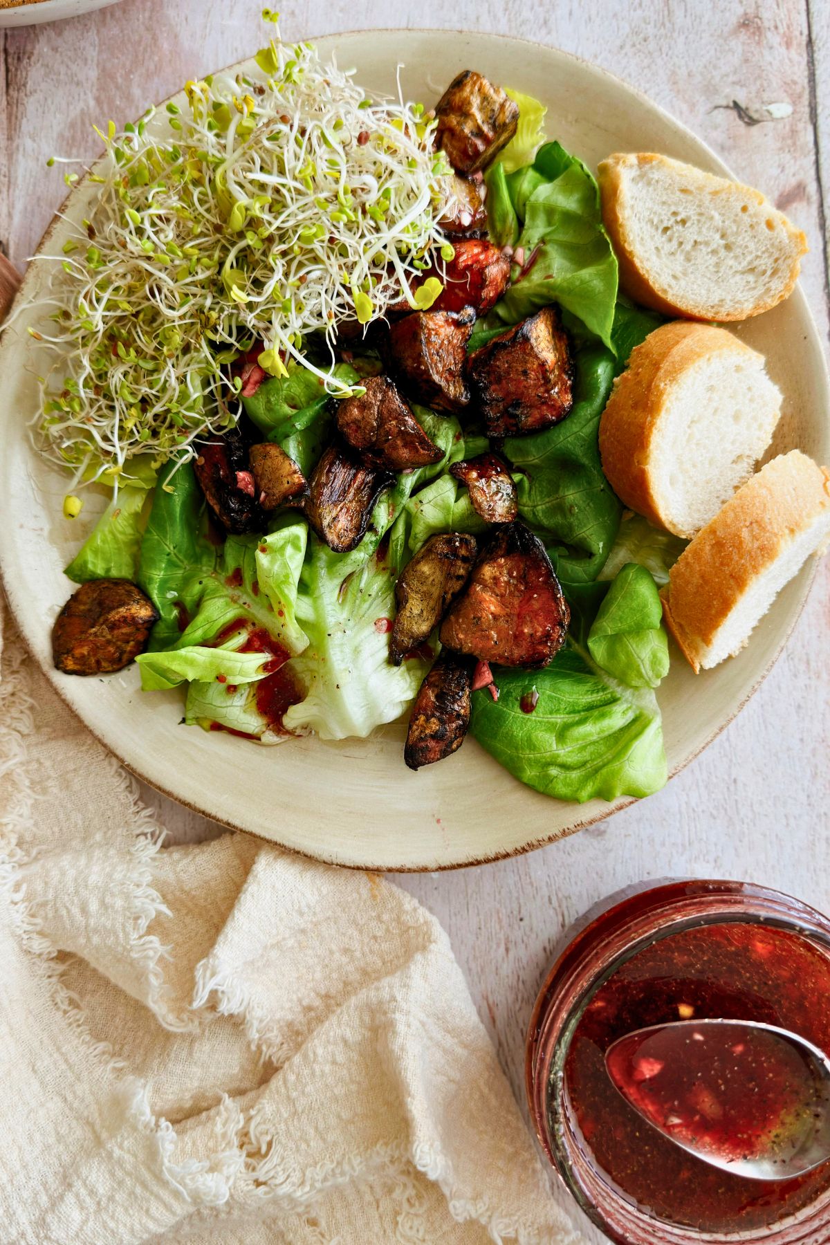 Butter lettuce salad topped with roasted vegetables and sprouts on a ceramic plate, with a jar of pomegranate molasses vinaigrette and crusty bread on the side.