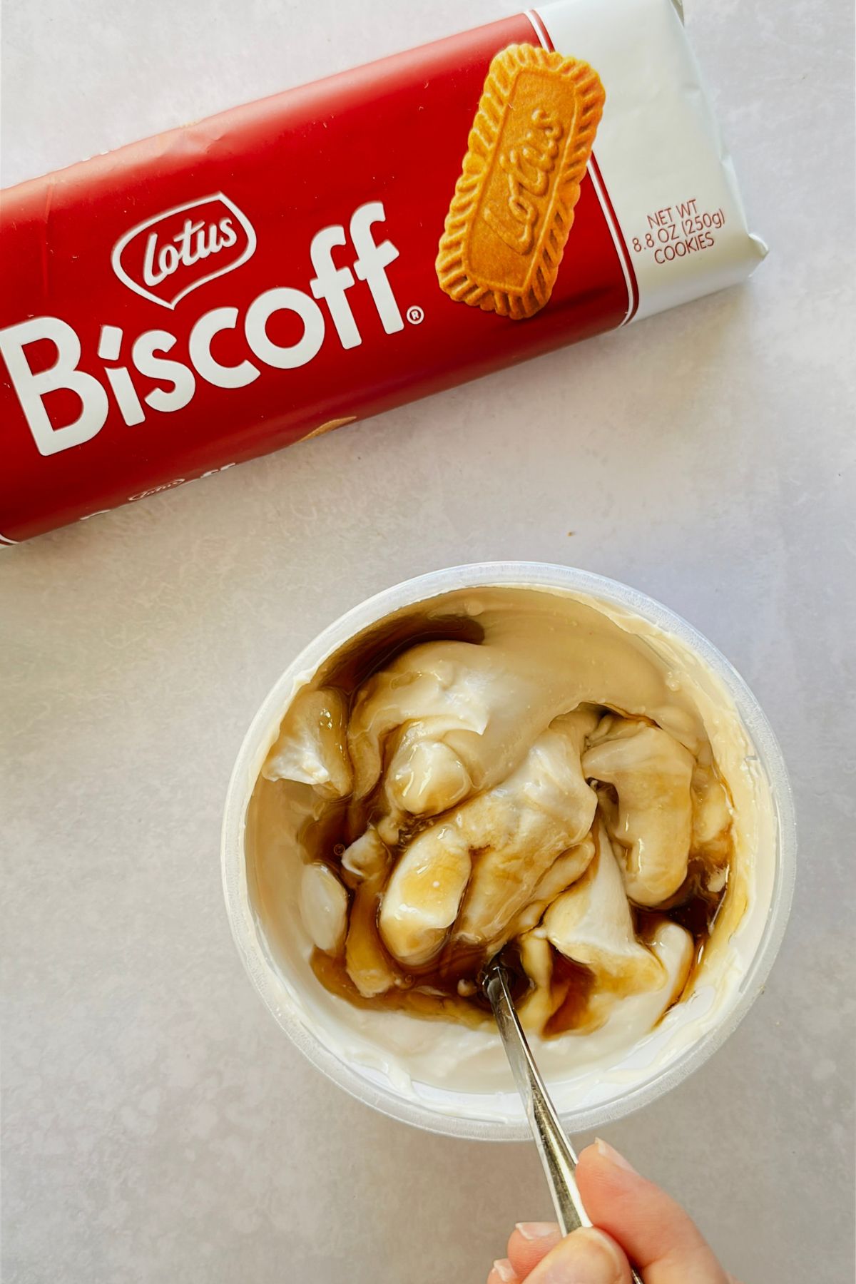 Overhead view of Biscoff cookies and Greek vegan yogurt, being stirred with a spoon.