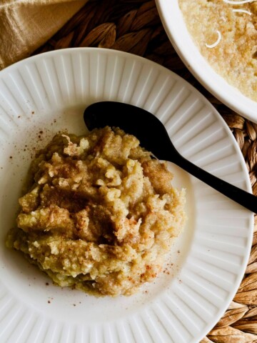 Boniatillo con coco topped with shredded coconut and cinnamon in a white bowl, with the serving dish in the background.