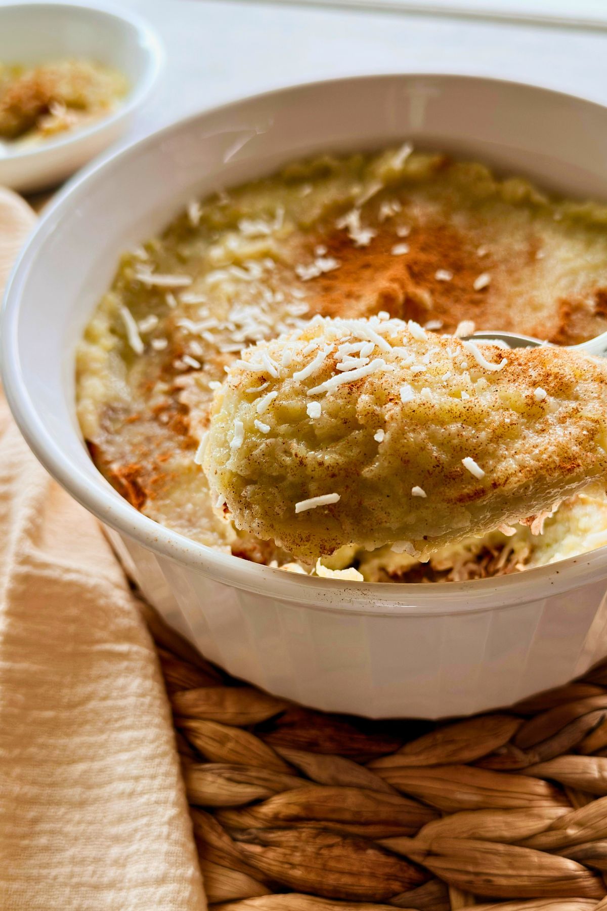 Spoonful of vegan boniatillo con coco lifted from a white serving dish, garnished with coconut flakes and cinnamon.