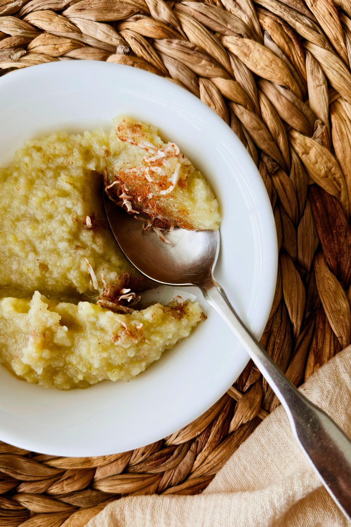 Boniatillo con coco in a white bowl topped with shredded coconut and cinnamon, spoon resting on top.