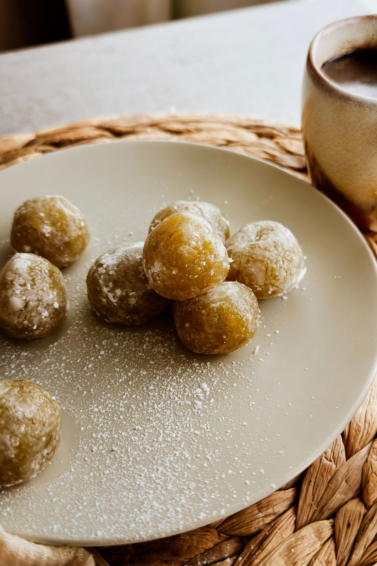 Boniatillo seco balls dusted with powdered sugar on a cream plate, served with Cuban coffee on a woven placemat.