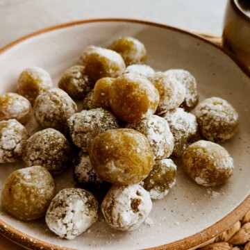 Close-up of boniatillo seco, a chewy Cuban sweet potato candy rolled in powdered sugar, mounded on a rustic speckled plate.