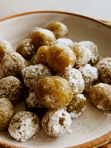 Close-up of boniatillo seco, a chewy Cuban sweet potato candy rolled in powdered sugar, mounded on a rustic speckled plate.