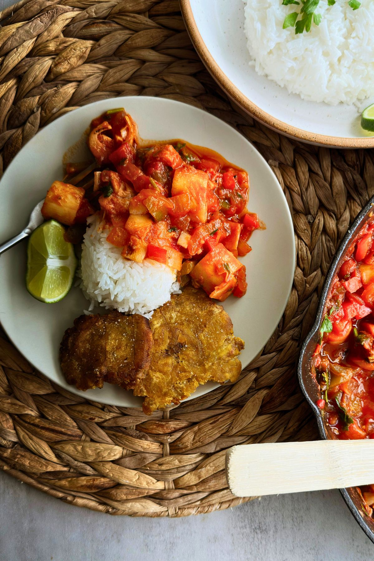Vegan camarones enchilados served over white rice with fried tostones and a lime wedge, on a woven placemat beside the cast iron skillet.