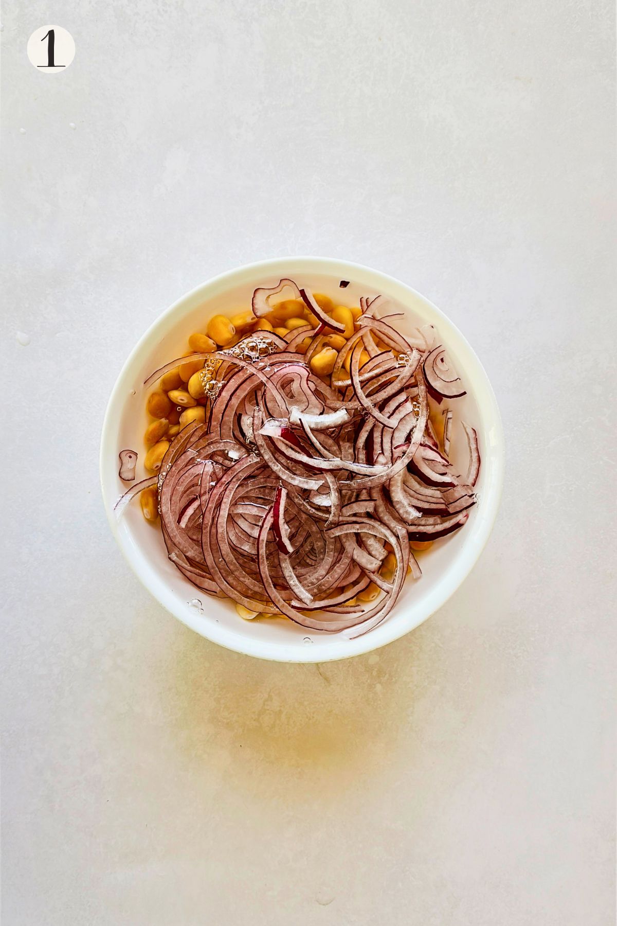 Step 1 of making ceviche de chochos: thinly sliced red onion and drained lupini beans soaking together in a bowl of cold water.