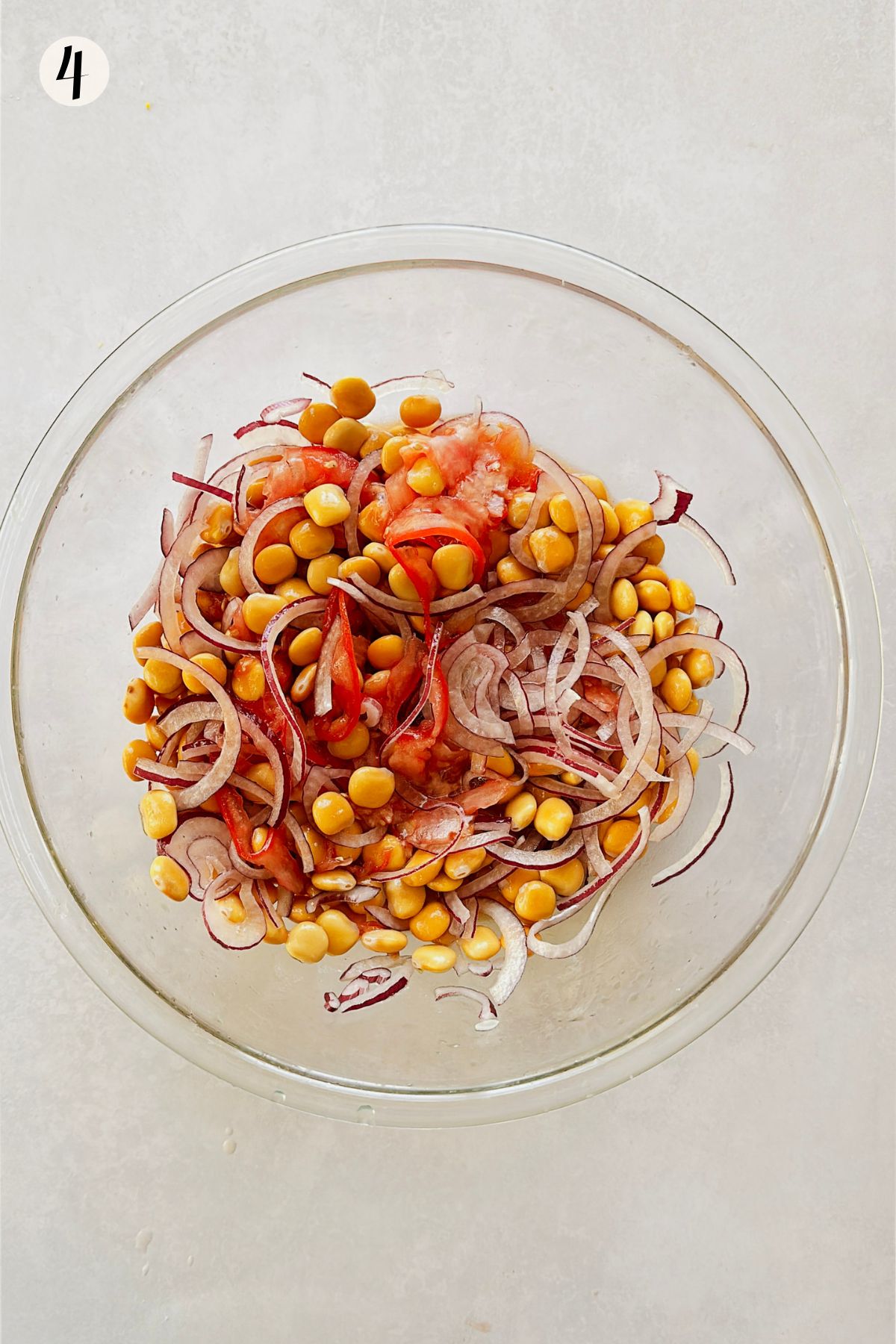 Step 4 of making ceviche de chochos: sliced tomato stirred into the lupini beans and red onion, everything coated in the coral-colored marinade.