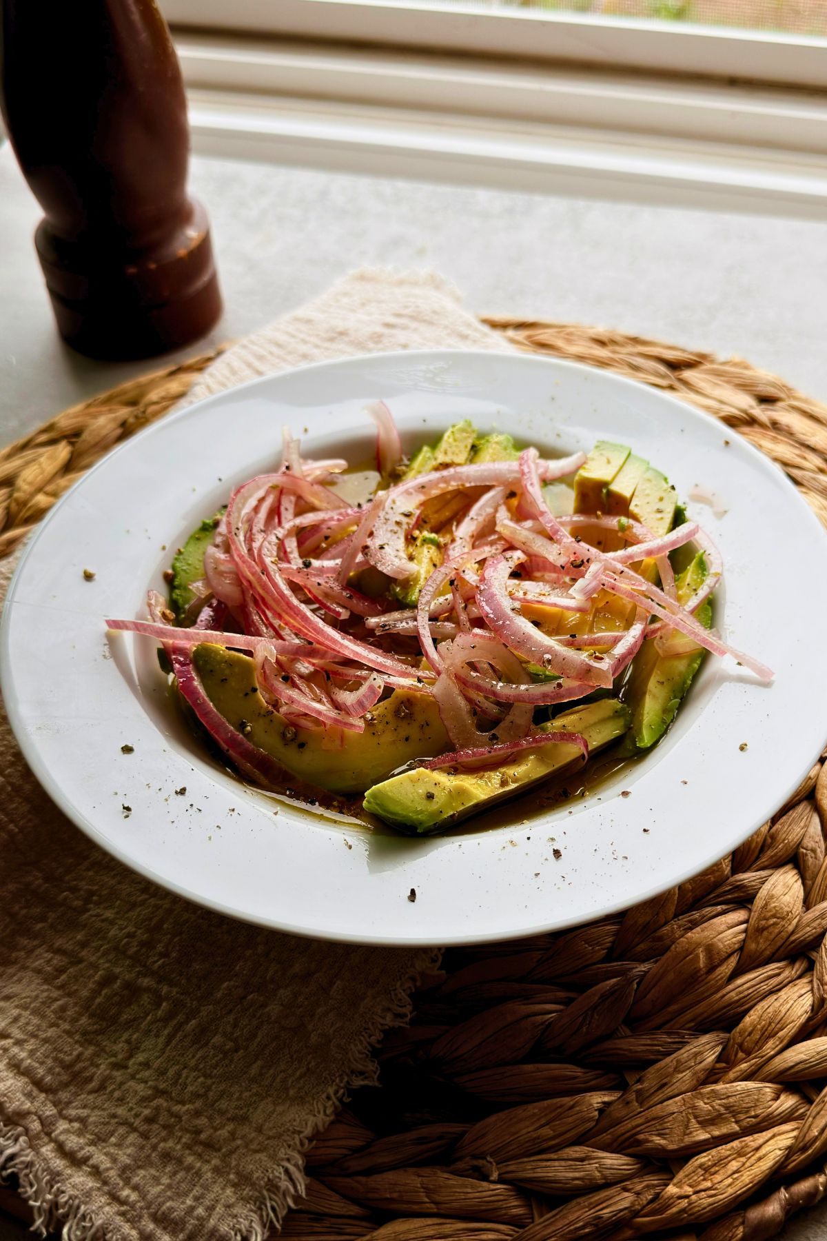 Cuban avocado salad with thin red onion on a white plate beside a pepper mill.