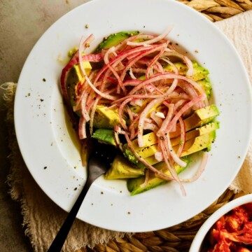 Overhead view of Cuban avocado salad with red onion and black pepper on the rim on a white plate.