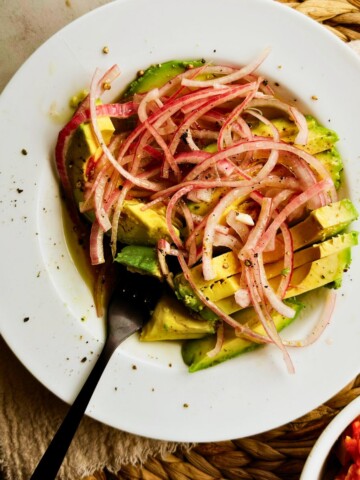 Overhead view of Cuban avocado salad with red onion and black pepper on the rim on a white plate.
