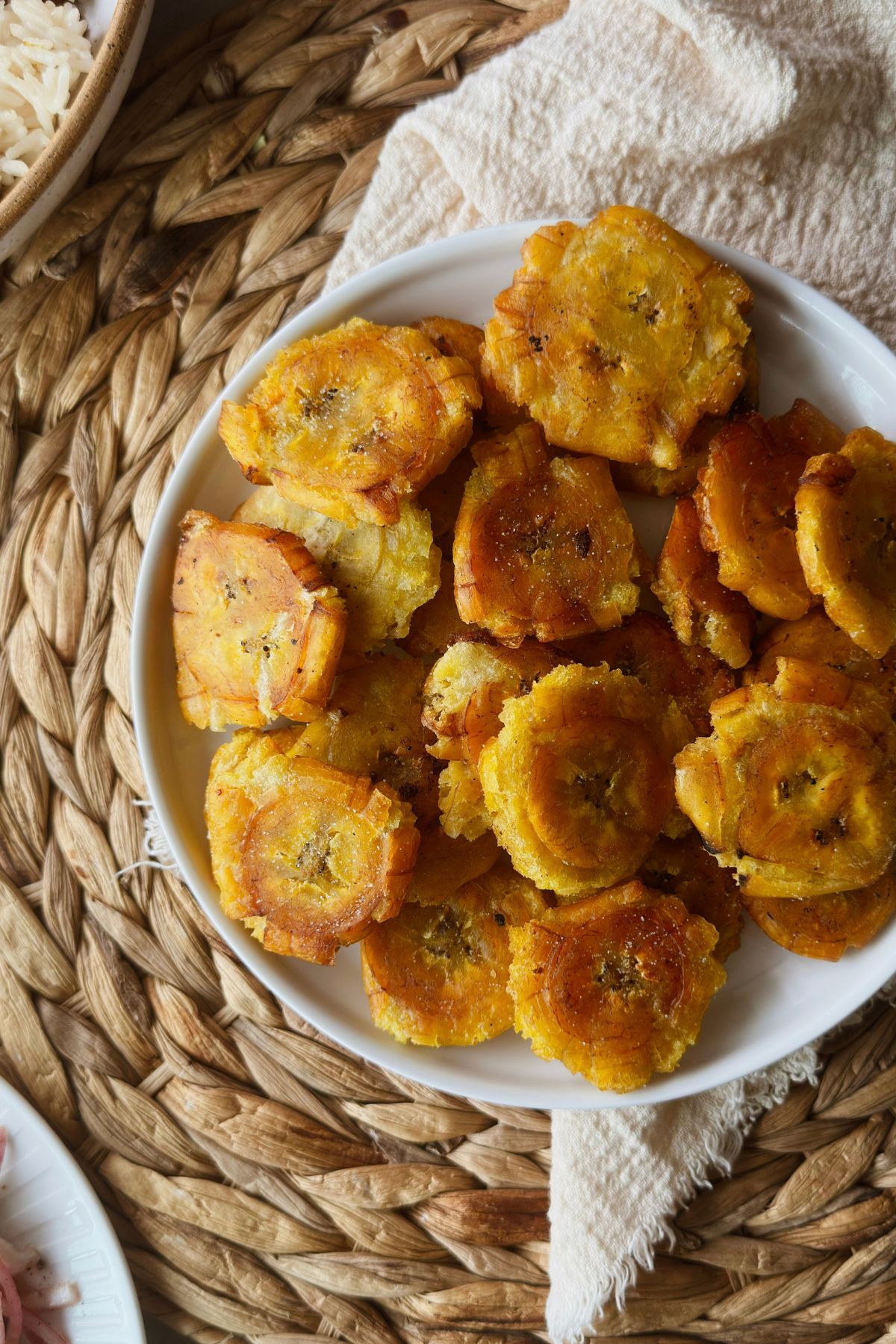 Golden tostones in a white bowl on a woven placemat.