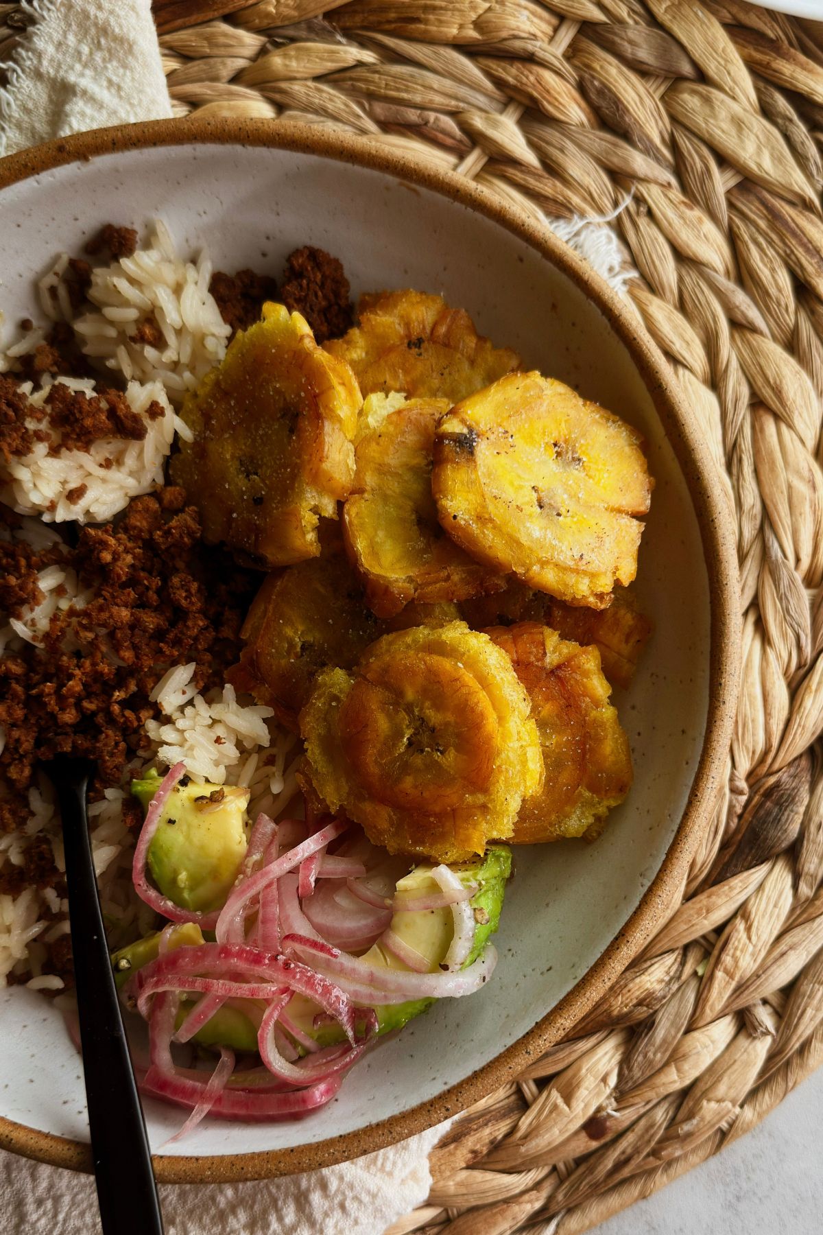 Tostones served with rice, vegan picadillo, avocado, and pickled red onions.