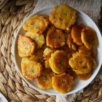 Golden tostones in a white bowl on a woven placemat.