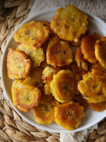 Golden tostones in a white bowl on a woven placemat.