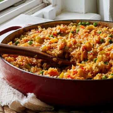 Red Dutch oven filled with vegan arroz con pollo, with wooden serving spoons resting in the golden rice.