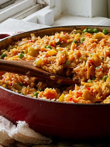 Red Dutch oven filled with vegan arroz con pollo, with wooden serving spoons resting in the golden rice.