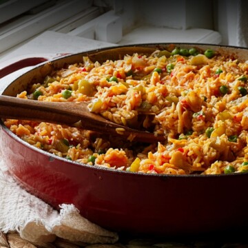 Red Dutch oven filled with vegan arroz con pollo, with wooden serving spoons resting in the golden rice.
