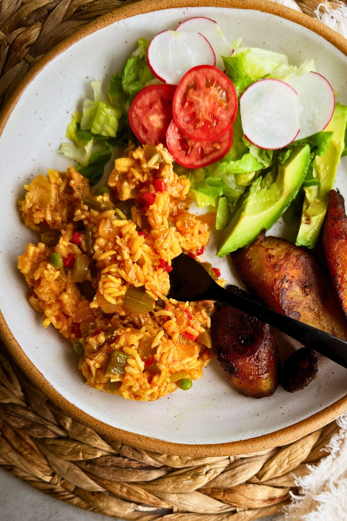 Vegan arroz con pollo served on a speckled stoneware plate with fried sweet plantains, avocado slices, tomato, radish, and lettuce salad.