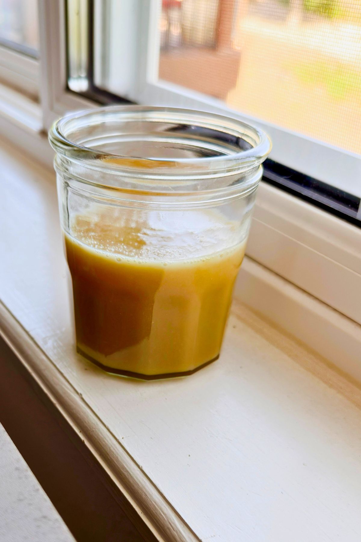 Jar of golden vegan sweetened condensed milk cooling on a windowsill.