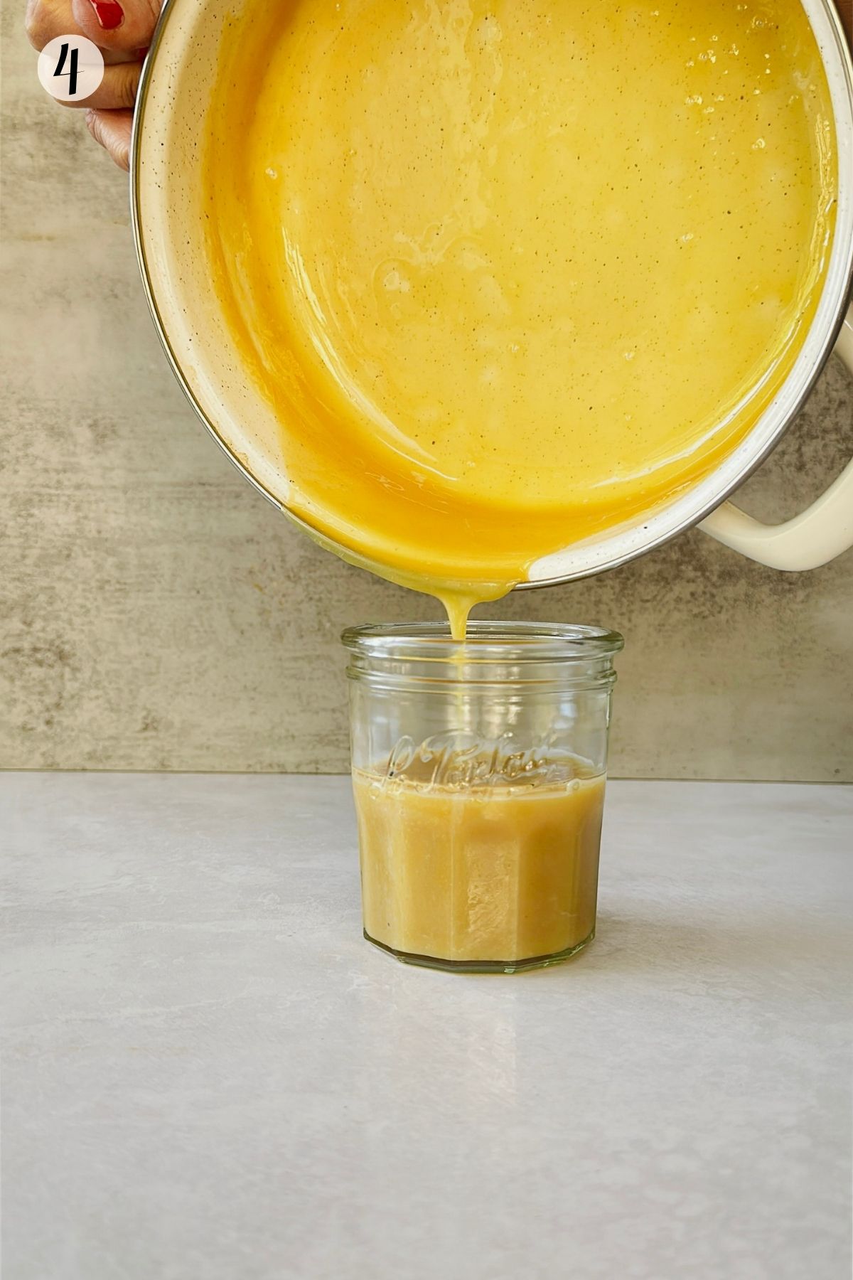 Step 4: Thick golden vegan condensed milk is poured from a saucepan into a clear glass jar.