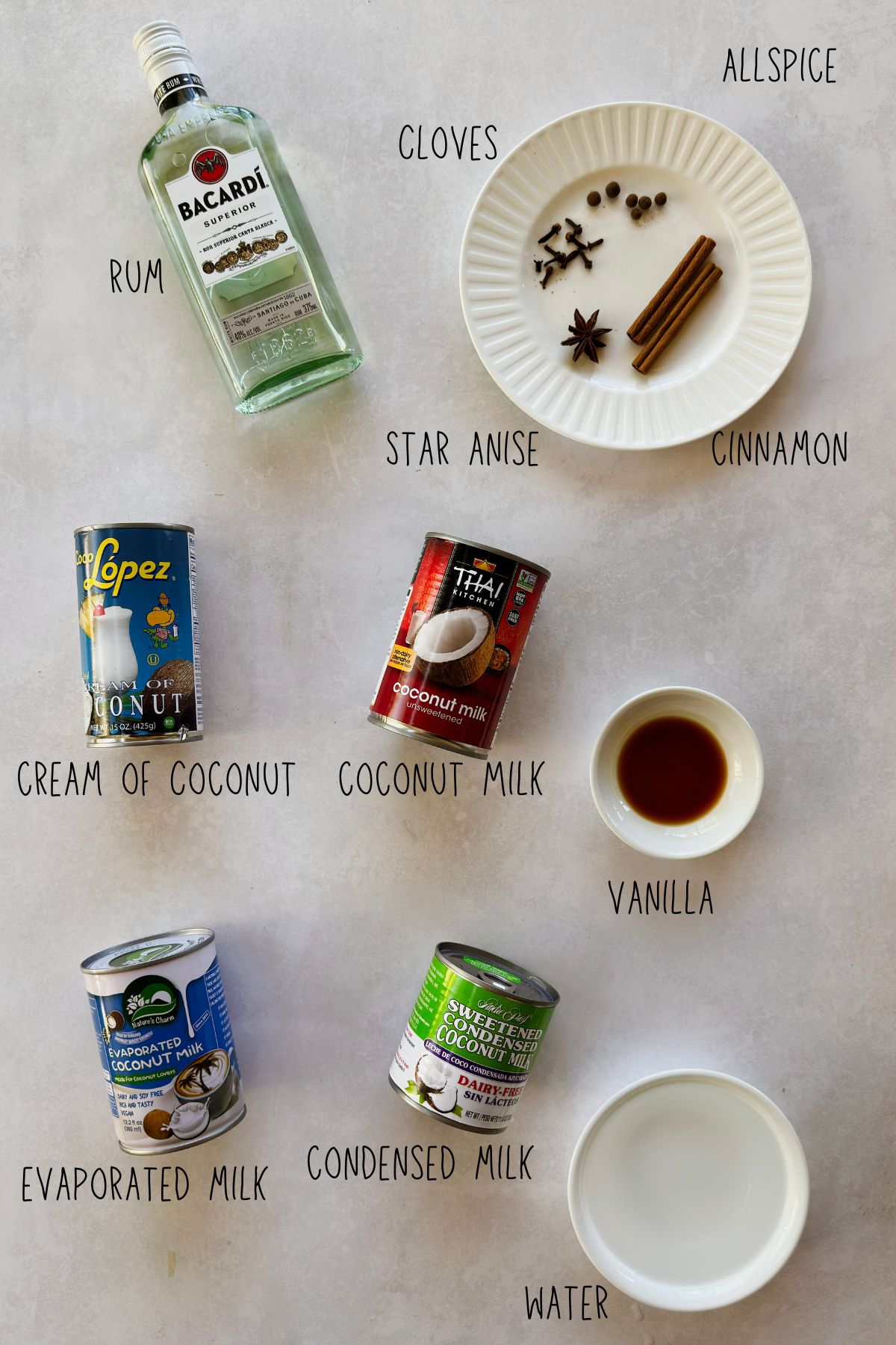 Ingredients for vegan coquito: rum, cream of coconut, coconut milk, evaporated and condensed coconut milks, vanilla, water, cinnamon sticks, cloves, star anise, and allspice.
