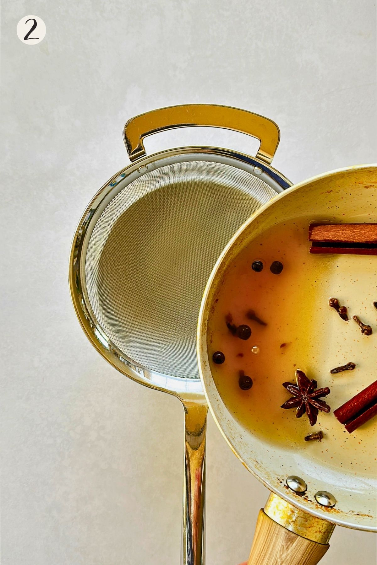 Step 2: Amber spice tea with cinnamon sticks, cloves, star anise, and allspice is poured through a fine-mesh strainer.