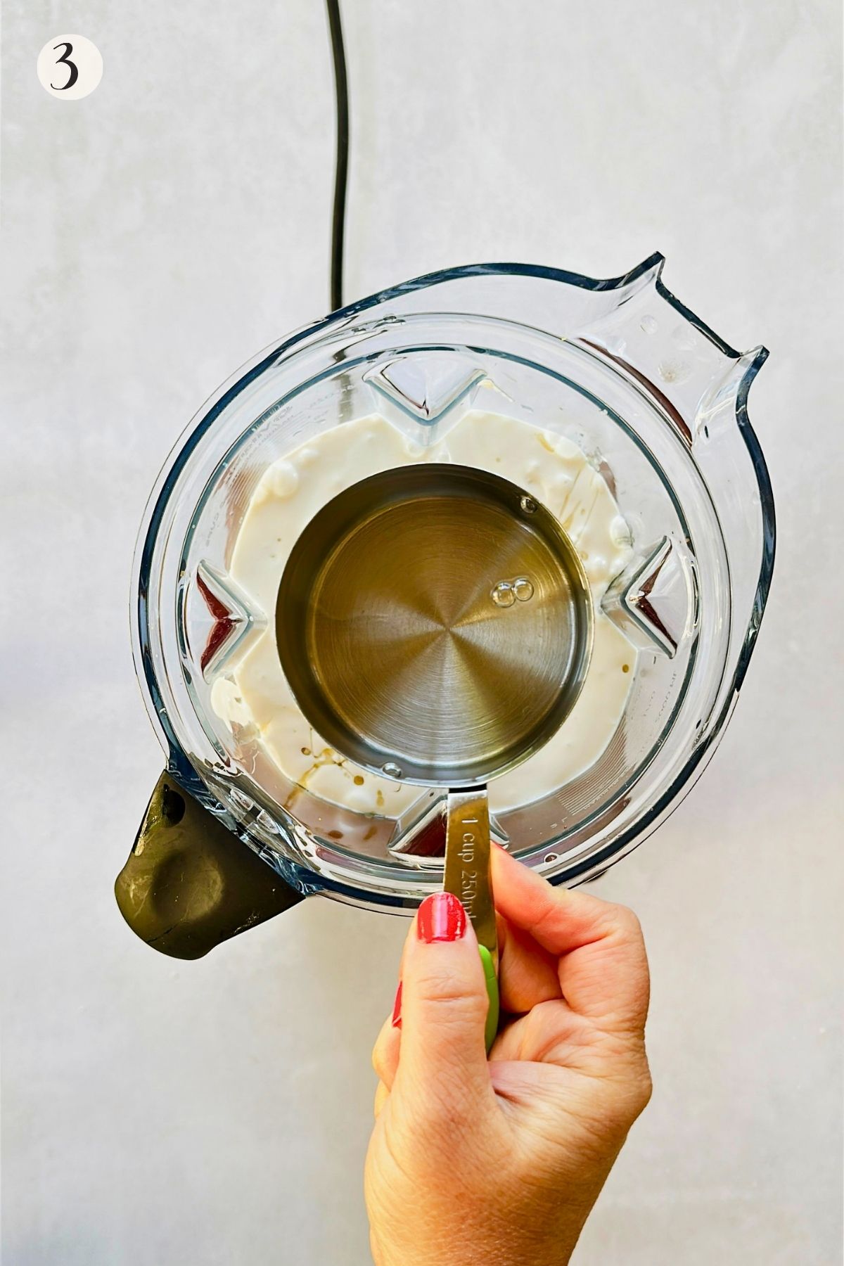 Step 3: A one-cup measure of rum is held over a blender filled with the creamy coconut mixture.