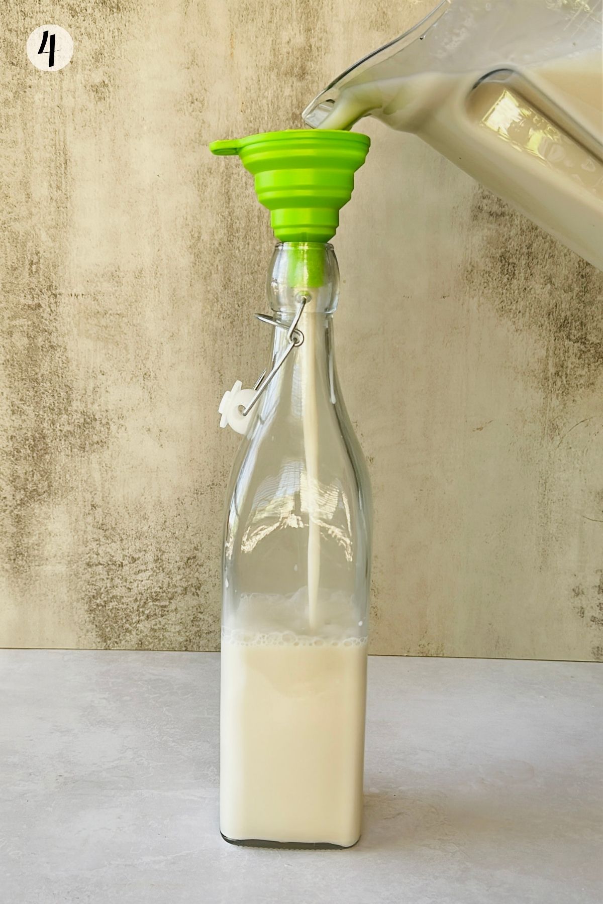 Step 4: Creamy coquito is poured from a blender through a green funnel into a clear swing-top bottle.
