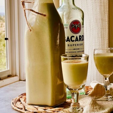 Vegan crema de vie in a swing-top bottle with two cordial glasses and a bottle of white rum.