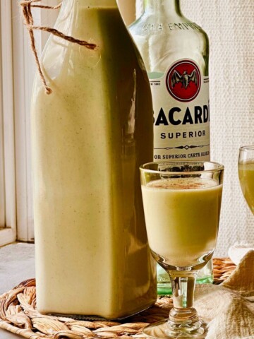 Vegan crema de vie in a swing-top bottle with two cordial glasses and a bottle of white rum.