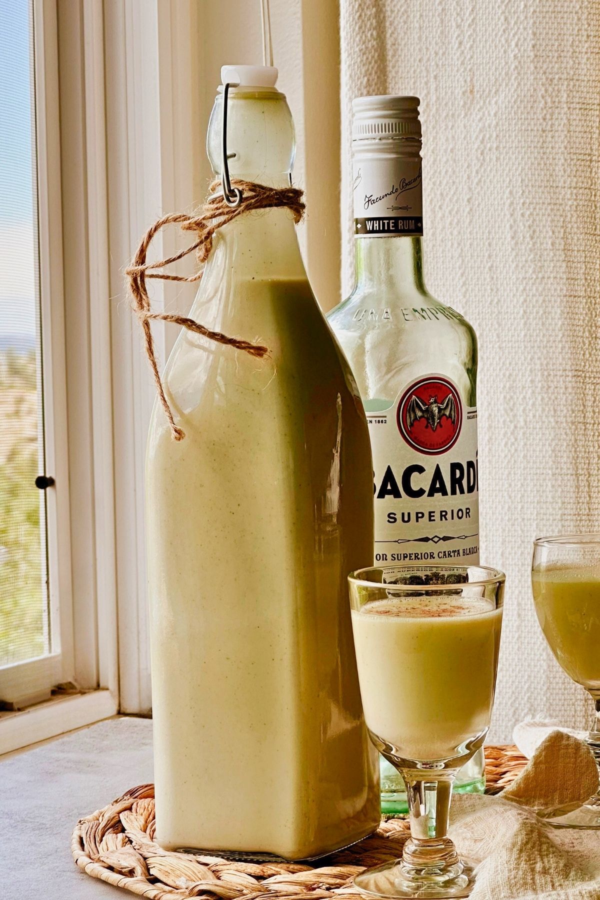 Vegan crema de vie in a swing-top bottle and cinnamon-dusted cordial glass beside white rum.