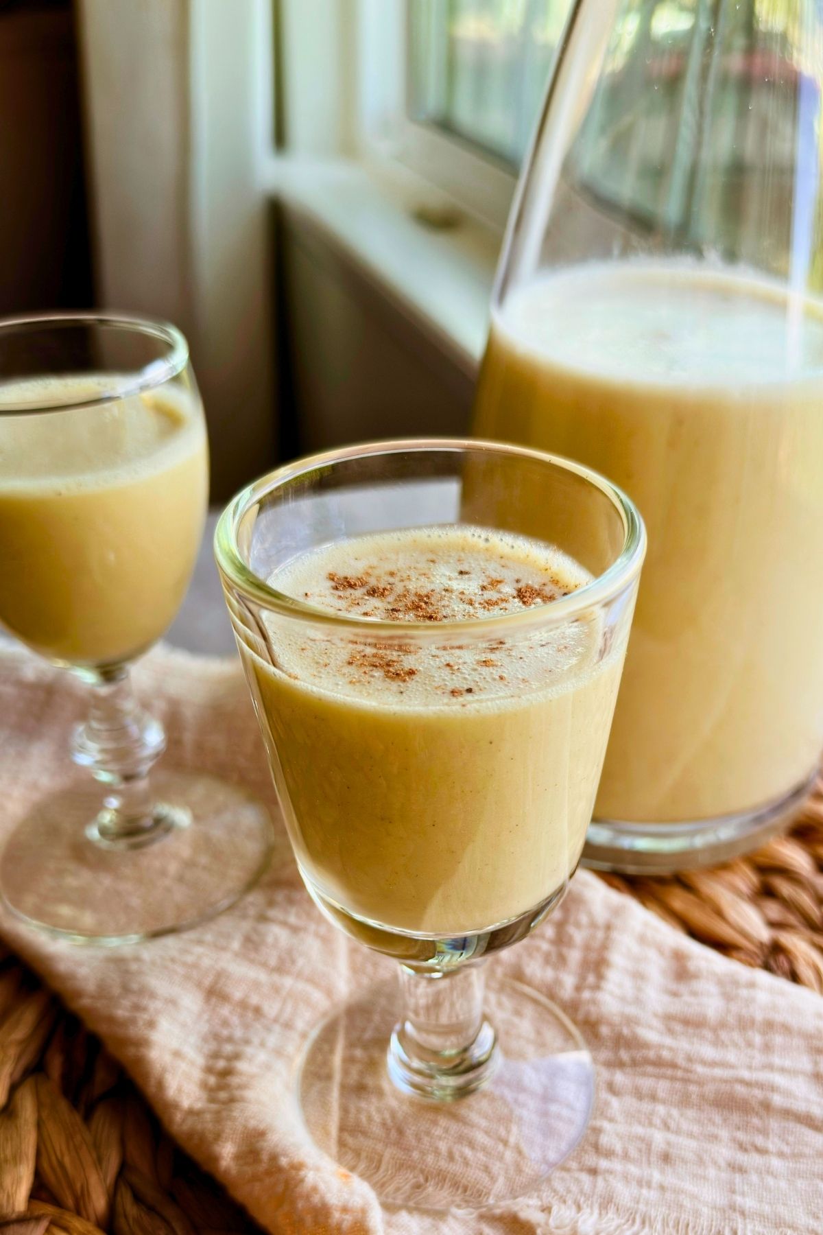 Two glasses of cinnamon-dusted vegan crema de vie beside a glass pitcher.