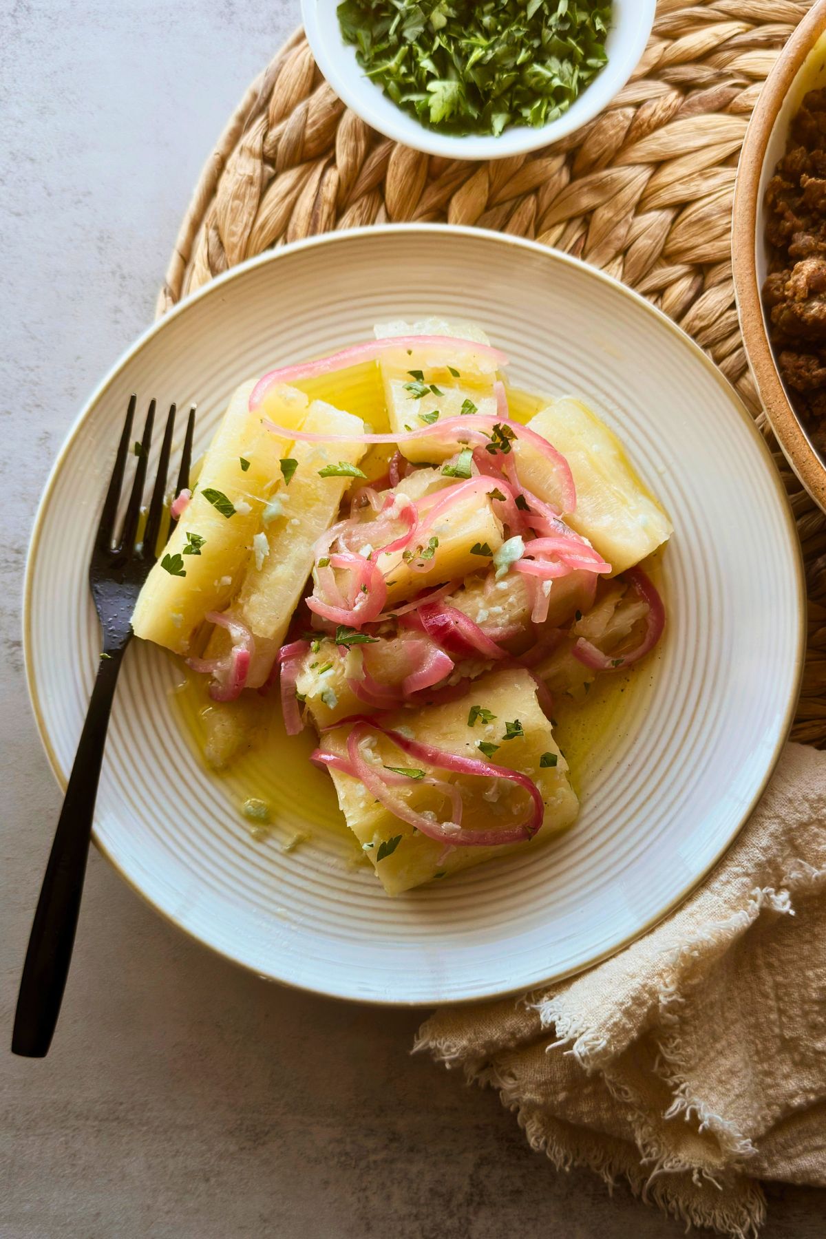 Yuca con mojo with pink onions and parsley on a white plate beside a black fork.