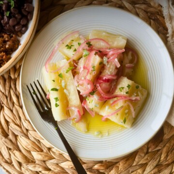 Yuca con mojo with pink onions and parsley on a white plate over a woven placemat.