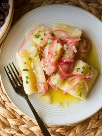 Yuca con mojo with pink onions and parsley on a white plate over a woven placemat.